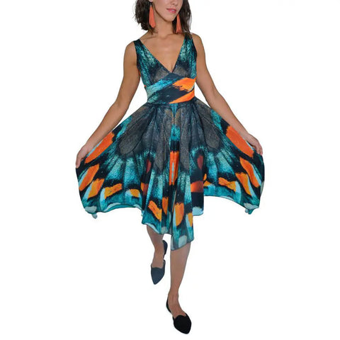 A woman showcases the Mt. Pisgah Butterfly Dress by Spiritex | Sustainable Apparel, featuring a vibrant blue, orange, and black butterfly wing pattern. She completes the look with black flats and orange earrings.