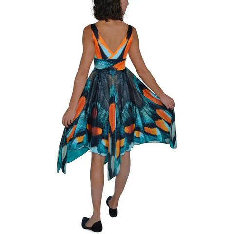 A woman stands with her back to the camera, spreading the sides of the Mt. Pisgah Butterfly Dress by Spiritex | Sustainable Apparel, a sleeveless sundress with butterfly wing design against a white background.
