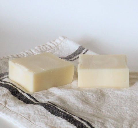 Two rectangular bars of White Leather Tallow’s Handmade Tallow Soap rest on a folded white cloth with dark stripes, all set against a simple light background.