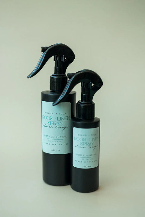 Two black bottles of Shanti + Tula’s Natural Room & Linen Spray – Odor Neutralizer & Air Refresher with light blue labels feature trigger tops, perfect for freshening your space. USA made and shown on a plain, light-colored background.