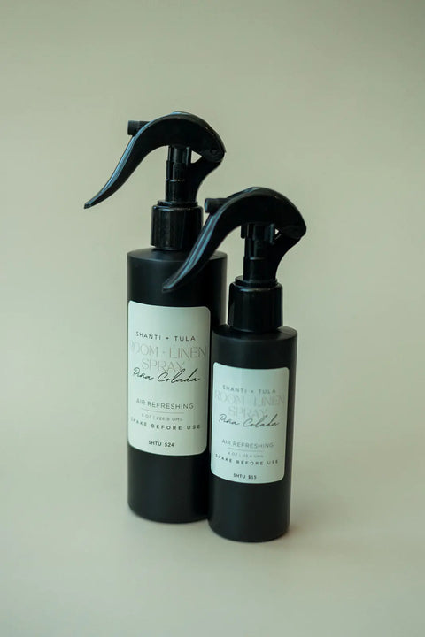 Two black bottles of Shanti + Tula Natural Room & Linen Spray – Odor Neutralizer & Air Refresher, featuring white labels with black text and trigger-style tops, stand on a neutral background. Made in the USA.