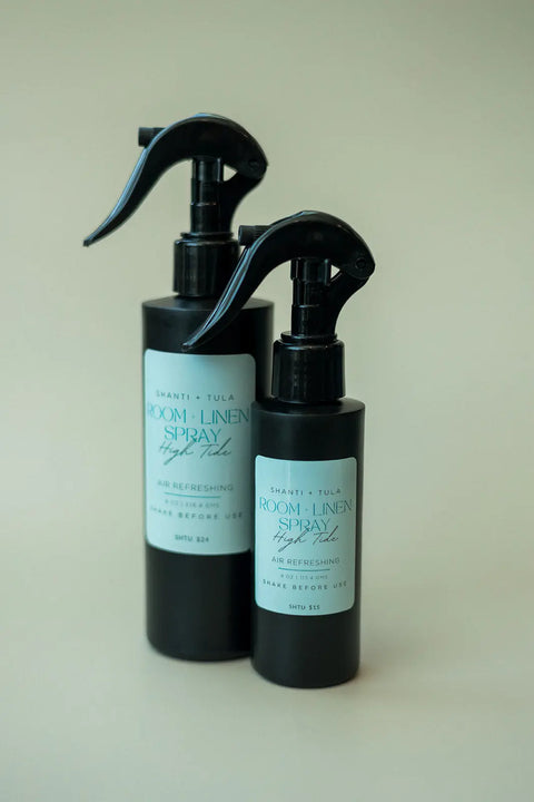 Two black Shanti + Tula Natural Room & Linen Spray bottles with trigger nozzles and light blue labels stand side by side on a neutral background—minimalist, USA-made, and perfect for refreshing and neutralizing odors in any space.