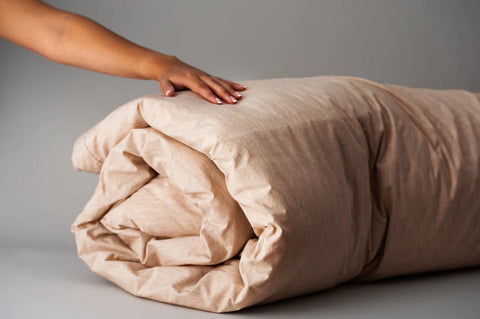 A hand gently rests on the Natural Colored Cotton Duvet Cover Set by American Blossom Linens, made from heirloom cotton, displayed against a plain gray background.