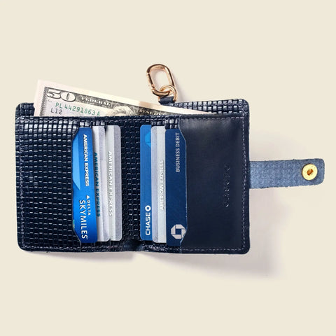 The CASUPO Wallet With Snap and Key Ring - Navy Limited Edition, made from sustainable leather, features a textured finish and snap closure. It’s displayed against a light beige background, holding cash and credit cards for style and functionality.