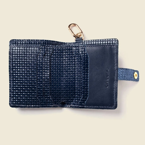 A textured navy handcrafted wallet, open to reveal multiple card slots, a snap closure strap, and a gold key ring at the top. The brand name CASUPO is embossed on the right side of this limited edition leather wallet.