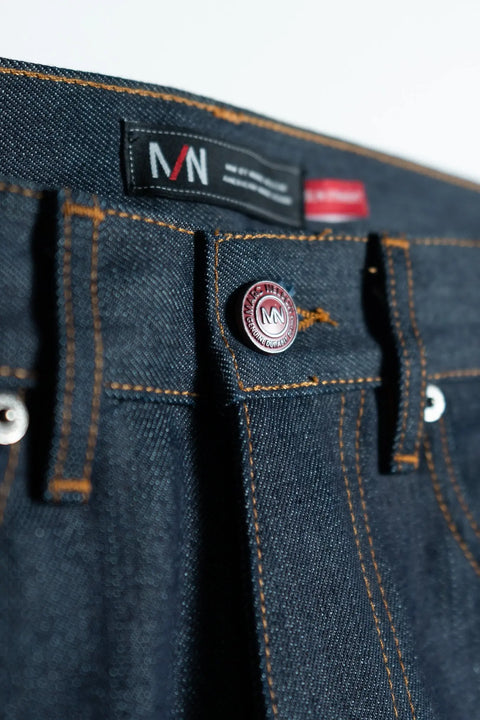 Close-up of the waistband on The Nelson Cone Mills Selvedge Denim by Marc Nelson, featuring orange stitching, a metal MN button, and a black MN label.