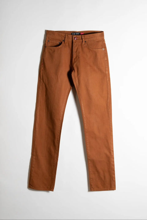 The Nelson Whiskey Stained Denim by Marc Nelson, a pair of slim straight jeans in rust-brown denim, laid flat on a white background.