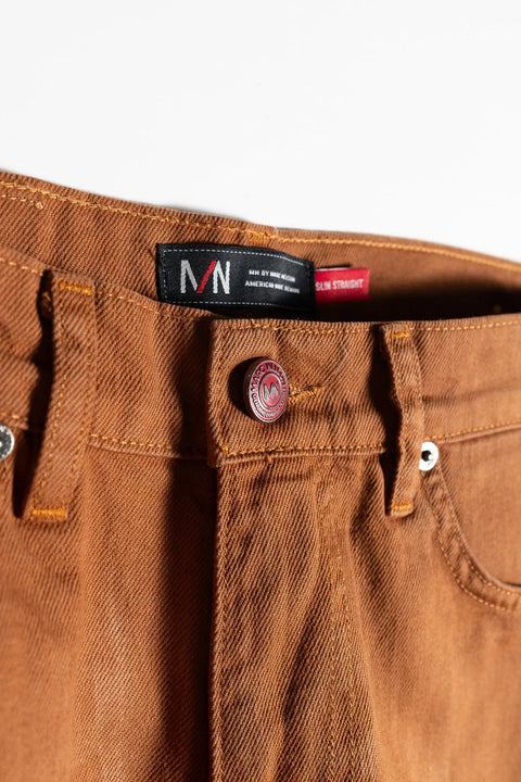 Close-up of the waistband and button on The Nelson Whiskey Stained Denim by Marc Nelson, featuring metal rivets, a red branded button, and a black label reading Slim Straight.