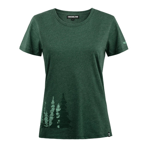 The Noble Fir - Pine women’s t-shirt by Fireside Pine comes in forest green, made in the USA, with pine tree silhouettes near the bottom left hem, a small logo on the left sleeve, and a Fresh Pine neck label.