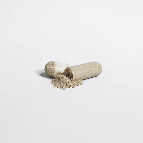 A beige gelatin capsule of Norri Nutrition’s Acai Detox supplement lies open on a white surface, with some light brown powder spilled out in front, highlighting its potential as a detox and weight loss aid.