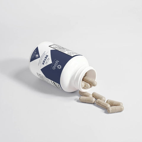 A white bottle labeled Norri Nutrition Acai Detox, a detox supplement, lies on its side on a light surface with several beige capsules spilling out of the open lid.