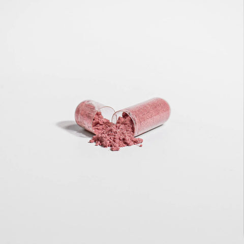 A transparent capsule of Norri Nutritions Beetroot supplement lies open on a white surface, releasing fine pink powder known for supporting cardiovascular wellness.
