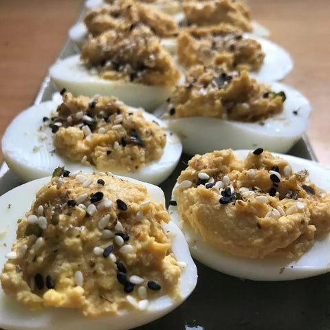 A close-up of deviled eggs in rows, topped with creamy yellow filling and sprinkled with Oceans Balance Bonito Furikake and black and white sesame seeds.