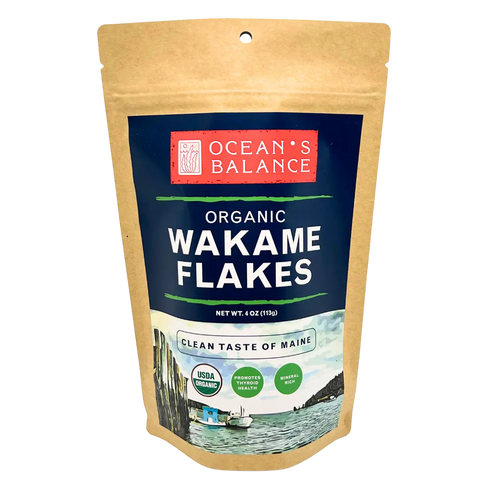 A resealable brown pouch labeled Oceans Balance Organic Wakame Flakes features Gulf of Maine coast art. The USDA Organic seaweed highlights its mineral-rich content. Net weight: 4 oz (113g).