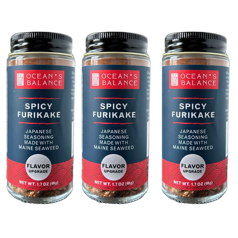 Three jars of Oceans Balance Spicy Furikake, a Japanese-style seasoning made with Maine seaweed, are arranged side by side against a black background. Each jar displays a bold red and navy label.
