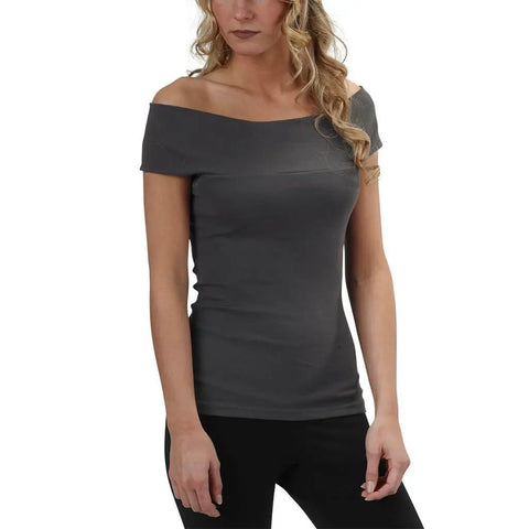 A woman with wavy blonde hair wears the Spiritex Venus Top in gray organic cotton, featuring an off-shoulder neckline, paired with black pants against a plain white background.