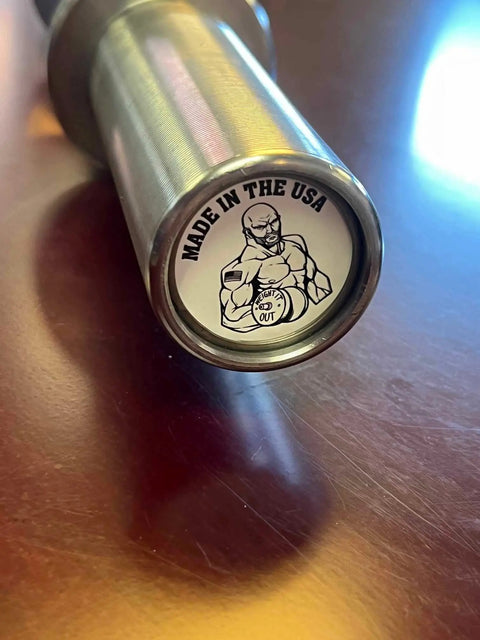 Close-up of a Weight It Out Premium Olympic Loadable Solid Steel Set (Of 2) Dumbbells end cap, featuring a muscular figure holding a barbell and MADE IN THE USA, shown on a reflective surface with bright zinc shaft and hard chrome sleeve.