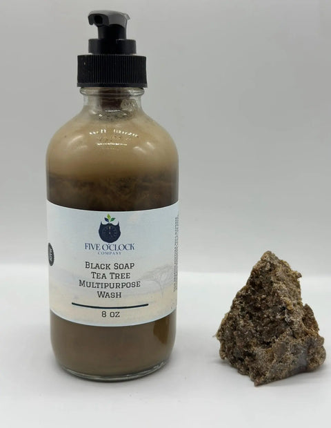 An 8oz bottle of Five O Clock Co. Black Soap and Tea Tree Face Wash with pump sits beside a piece of raw black soap—ideal for sensitive skin and eczema—set against a plain white background.