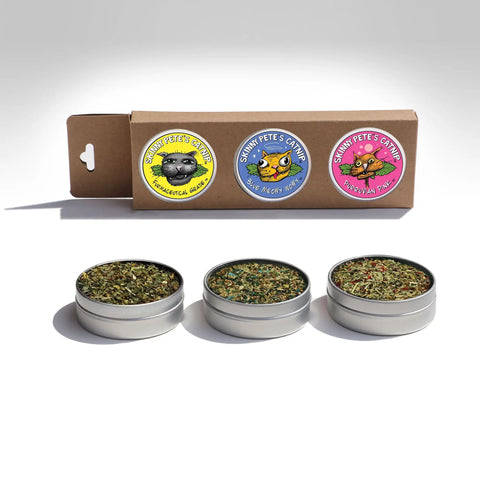 Three small tins of dried herbs from Skinny Petes Gourmet Catnip—featuring Pharmaceutical Grade, Wide-Open Work, and Himalayan Sun—come in a colorful box as the Three Piece Gourmet Catnip Gift Set.