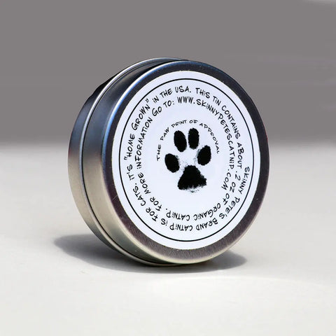 A small metal tin with a white label on the lid features a black paw print and details about Skinny Petes Gourmet Catnip. Shown on a neutral surface, this is part of the Three Piece Gourmet Catnip Gift Set for cats.