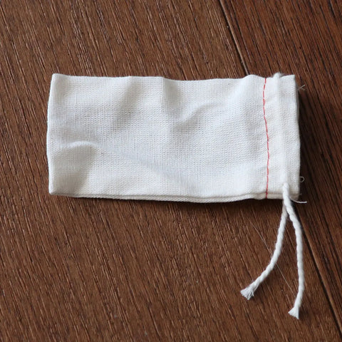 A small white cloth drawstring bag with red stitching from Skinny Petes Gourmet Catnip, part of the Three Piece Gourmet Catnip Gift Set, lies on a wooden surface—ideal as an organic catnip toy for cats.