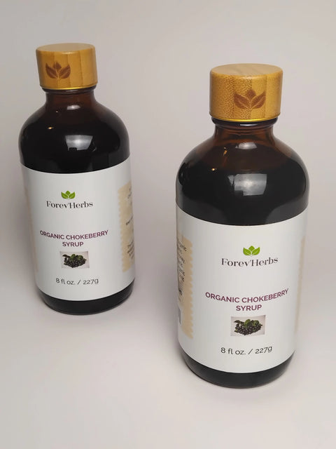Two bottles of Forev'Herbs Organic Chokeberry Syrup with white labels and bamboo-style caps, each 8 fl oz (227g), are shown against a plain white background.