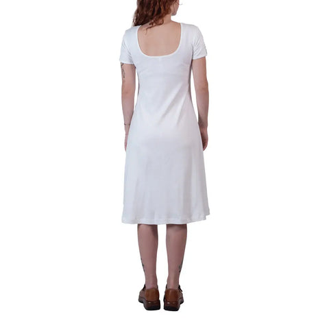 A person with wavy hair stands with their back to the camera, wearing the Spiritex | Sustainable Apparel Lake Shore Dress in white and brown shoes, set against a white background.