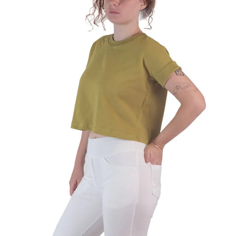 A woman wears the Spiritex | Sustainable Apparel Roan Crop Top in olive green, made from 100% organic cotton, paired with high-waisted white pants. She poses with one hand in her pocket against a plain white background, showcasing sustainable style.