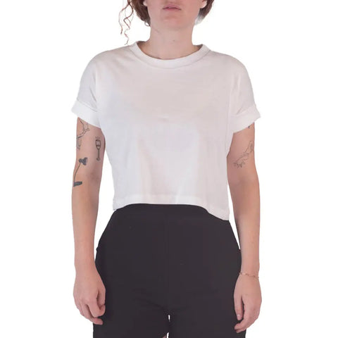 A person with light skin and curly hair wears the Roan Crop Top by Spiritex | Sustainable Apparel and black pants, showing tattoos on their arms against a white background—a showcase of sustainable fashion.