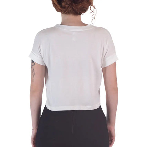 A person with curly hair is shown from the back, wearing the Spiritex | Sustainable Apparel Roan Crop Top made from 100% organic cotton and black pants. A small tattoo is visible on their left arm against a white background.
