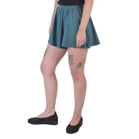 A person wearing Spiritex | Sustainable Apparel Drape Shorts, black shoes, and a black top stands against a white background, showcasing thigh tattoos—perfect summer wardrobe inspiration.