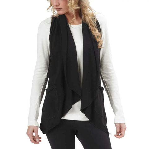 A woman with wavy blonde hair wears a white long-sleeve shirt, black pants, and the Ultra Lightweight Draped Vest by Spiritex | Sustainable Apparel, holding the sides of this chic layering piece while looking down to her left.