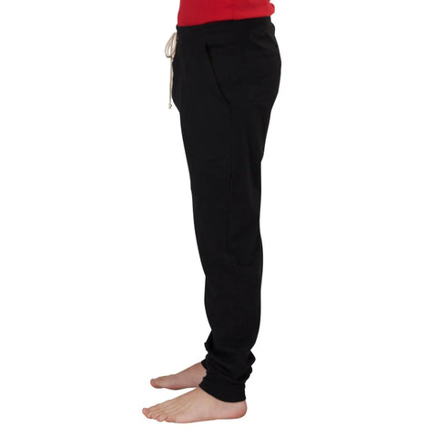 A person stands barefoot in side profile on a white background, wearing Spiritex | Sustainable Apparel Drawstring Jogger Pants in black organic cotton with a drawstring waistband and a red top.