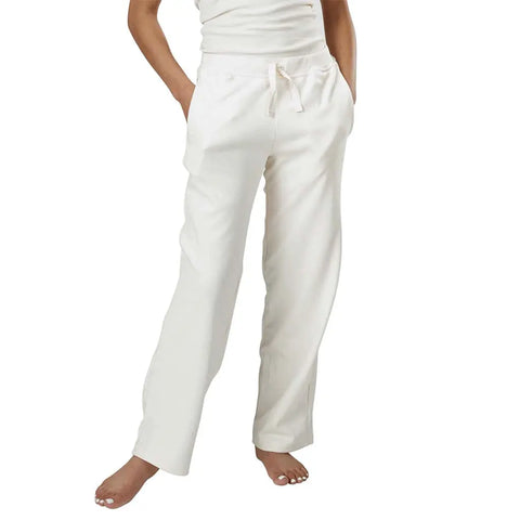 A barefoot person, shown from the waist down, wears off-white, loose-fitting Drawstring Lounge Pant by Spiritex | Sustainable Apparel, made from organic cotton and featuring a relaxed yoga pant style with hands in their pockets.