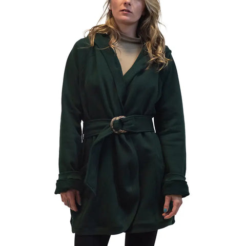 A woman stands against a white background wearing the Spiritex Fleece Wrap Jacket in dark green over a tan top and black pants. Her hands are relaxed at her sides, and her wavy blonde hair partly covers her face.