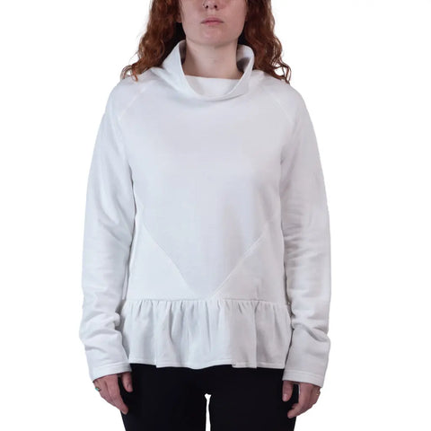 A person with long, curly hair wears the Charlotte Street Sweatshirt by Spiritex | Sustainable Apparel, featuring an oversized fit and ruffled hem, paired with black pants against a plain white background.