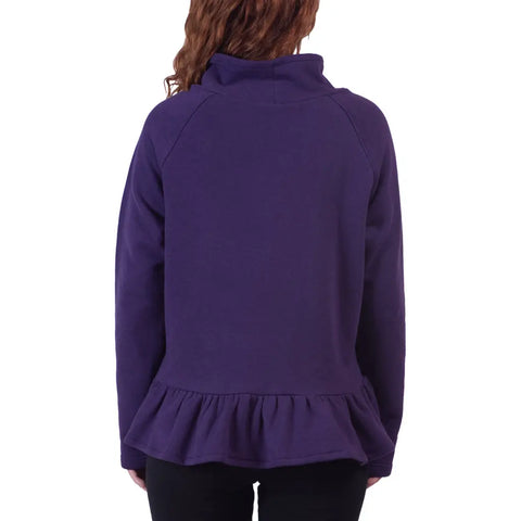 A person with wavy brown hair, seen from behind, is wearing the Charlotte Street Sweatshirt by Spiritex | Sustainable Apparel—a relaxed-fit, oversized purple turtleneck with a ruffled hem—paired with black pants.