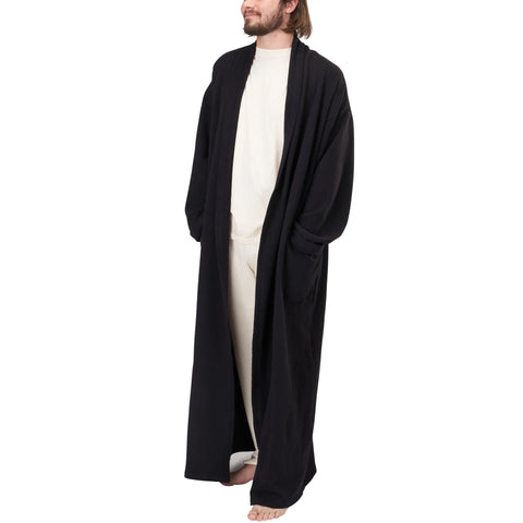 A man with light brown hair and a beard stands barefoot against a white background, wearing the Spiritex | Sustainable Apparel Full-Length Fleece Robe over loose, light-colored clothing.