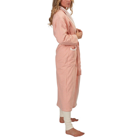 A woman stands barefoot in a side view, wearing the Spiritex | Sustainable Apparel Full-Length Fleece Robe in pink and white stripes over white leggings. She holds the robes belt, with wavy hair cascading over her shoulders.