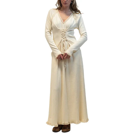 A woman wears the Spiritex | Sustainable Apparel Gwynne Dress, a long cream corset-inspired style with a lace-up front and long sleeves, standing against a plain white background.
