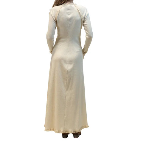 A person shown from the back wearing the Spiritex | Sustainable Apparel Gwynne Dress, a long-sleeved, cream organic cotton ankle-length dress with a subtle textured pattern and a slight flare at the hem.