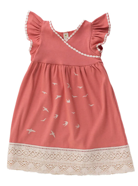 The Girls Bird Flock Dress by Spiritex | Sustainable Apparel is a coral pink organic cotton dress featuring ruffled sleeves, white scalloped trim, bird prints on the skirt, and a wide cream lace hem.