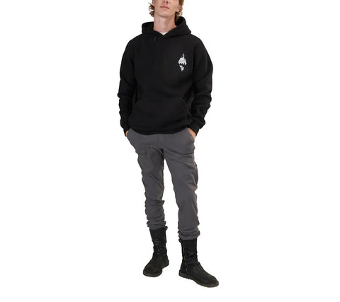 A person wears the Spiritex Graphic Heavyweight Fleece Hoodie | Mountain Scape—black with a small white chest graphic—paired with gray pants and black boots, standing hands-in-pockets against a plain white background.