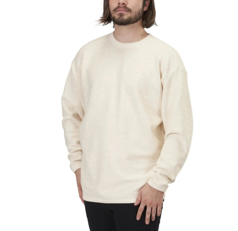 A man with shoulder-length hair and a beard wears the Spiritex Herringbone Drop Shoulder Crewneck Sweatshirt in cream and black pants, standing against a plain white background.
