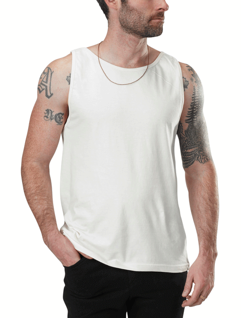 A tattooed man wears the Spiritex | Sustainable Apparel Jersey Tank in plain white, made from 100% organic cotton, paired with a thin chain necklace and black pants. He looks to the side with one hand in his pocket.