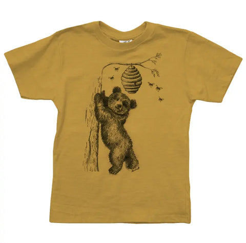 The Honey Bear Graphic Tee by Spiritex | Sustainable Apparel is a mustard yellow organic cotton kids’ shirt featuring a bear cub reaching for a beehive with buzzing bees.