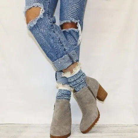 Person wearing light gray suede ankle boots, Catherine Cole ORGANIC Lace Boot Socks - Denim Blue, and ripped, rolled-up blue jeans stands against a white background.