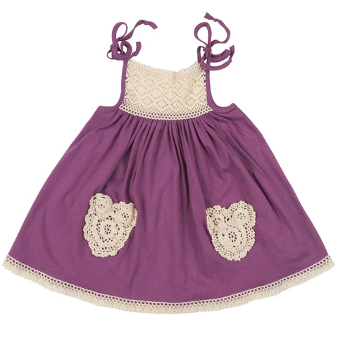 The Lace Pocket Dress by Spiritex | Sustainable Apparel is a purple organic cotton A-line toddler dress with cream crochet trim, heart-shaped front pockets, shoulder ties, and a gathered skirt.