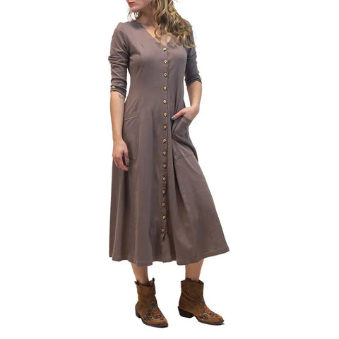 A woman wears the Spiritex Leaf Dress, a long-sleeved brown autumn dress with pockets, standing with one hand in her pocket and paired with embroidered brown ankle boots.