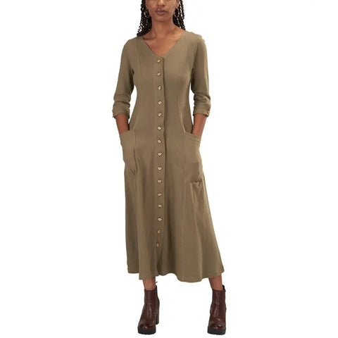 A woman in the Spiritex | Sustainable Apparel Leaf Dress, a long-sleeved olive green organic cotton button-down with side pockets, paired with brown ankle boots, stands against a white background.